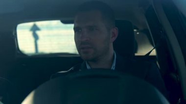 Handsome young businessman sitting in the car and driving. Caucasian man in suit drives his car to work. Close up. Business people. Man driver inside vehicle. Transportation, traffic, trip concept