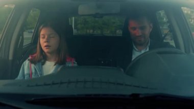 Pretty Caucasian teenager female sitting in car in front seat. Cheerful handsome man waiting in car little girl. Young dad picks up child driving vehicle. Family, childhood. Slow motion, Close up