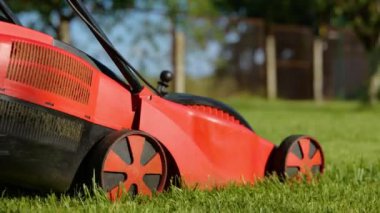 Side view of lawn-mower machine cutting grass outdoors in garden. Close up of an electric lawn mower mows lawn in the backyard. Garden care. Nature and landscape. Slow motion. Gardening concept