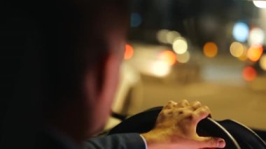 Direksiyondaki erkek eli yakından çek. Geceleri araba süren bir adam. Gösterge paneli. Şehir ışıkları akşam bulanık arka planda. Lüks bir yaşam tarzı. Seyahat, gezi. Gece hayatı konsepti