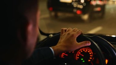 Gece şehir caddesinde trafikte hızlı araba kullanan bir adam. Yolculuk, hız, sürücü konsepti. Banliyö, taksi şoförü erkek. Arabanın direksiyonundaki erkek elinin iç görünüşü. Kapat.