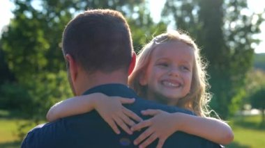 Close up of joyful little girl laughing hugging her dad outdoors in park. Family concept. Rear of male parent holding his small child on hands on sunny day. Positive emotions. Happy childhood