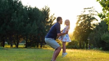 Happy young Caucasian man playing with little pretty daughter on nature. Cheerful loving dad spinning his cute child girl in park. Kid having fun outdoors with father. Family day. Leisure concept