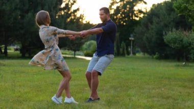 Happy couple having fun in green park holding hands and spinning looking at each other. Young Caucasian man and woman in love outdoors. Boyfriend and girlfriend. Nature landscape. Romantic concept