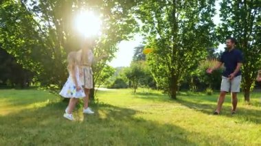 Caucasian family throwing frisbee disk in park on sunny day. Smiling girls jumping cheering for parents while mom and dad play with frisbee plate. Children and parents fun. Summer outdoor activity