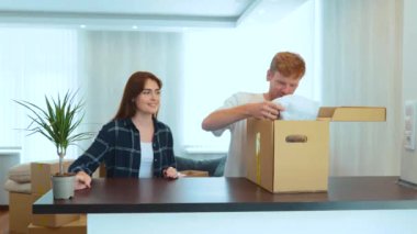 Portrait of young married couple settled down living together in new home. Couple unpacking stuff from cardboard box after moving in a new apartment. Happy spouses purchased flat. Moving day concept