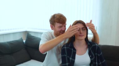 Camera moving back from young happy couple sitting on sofa in new apartment with many boxes. Relocation concept. Moving in together. Marriage mortgage. Husband surprised his beloved wife in new home