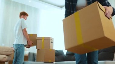 Close up of joyful positive young man and woman indoors in room with many boxes putting stuff on floor. Married couple with cardboard boxes in new apartment. Relocation. Slow motion. Moving day