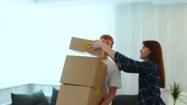 Close up of young Caucasian red-haired guy holding many cardboard boxes in hands and woman putting another one on top. Couple moving from the apartment. Relocation concept. Family moves. Slow motion