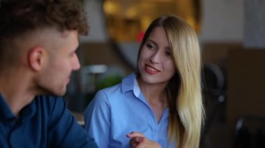 Close up of Caucasian handsome man and pretty woman speaking while sitting in restaurant and using laptop browsing online. Young people discussing something and typing on computer in cafeteria