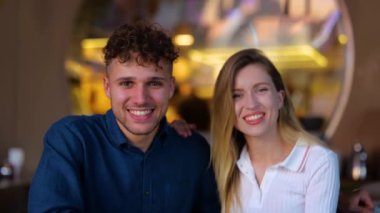Close up portrait of young happy male and female couple sitting in bar and waving hands speaking to camera. Joyful boyfriend and girlfriend on a date. Conversation. Communication concept. Slow motion