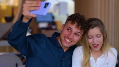 Close up of young happy positive couple on a date taking selfie photo while eating pasta in restaurant. Cheerful male and female couple in love posing to smartphone camera. Fun. Dating concept