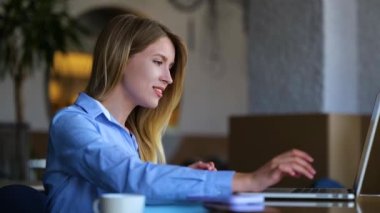 Close up of cheerful beautiful businesswoman typing on laptop sitting in restaurant then looking at camera and smiling. Slow motion. Caucasian young female working in cafeteria. Business concept