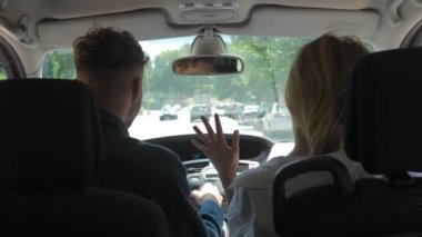 Rear of happy young couple man and woman sitting in car having a trip together. Back view of Caucasian cheerful girlfriend dancing having fun in auto during travel with her boyfriend. Journey concept