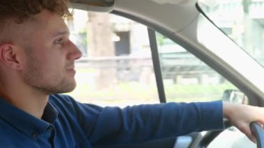 Side view of Caucasian handsome joyful guy driver sitting in car with his hands on steering wheel driving a vehicle in city. Close up. Happy young man goes to work in own auto.Transportation concept