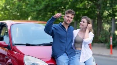 Caucasian married couple man and woman have bought a new red car. Portrait of joyful positive boyfriend and girlfriend showing keys to their new vehicle. Transport. New automobile concept
