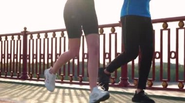 Close up of people legs in sportswear running on street outdoors on bridge. Male and female run together outside on summer day. Man and woman legs jogging. Sport lifestyle. Healthy active concept