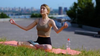 Caucasian young pretty woman meditating in nature on sunny summer day breathing deeply and calm. Slow motion. Healthy active lifestyle. Beautiful contented female athlete working out practicing yoga