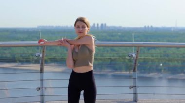 Beautiful slim woman having workout outdoors stretching muscles standing outdoor on bridge with view on river. Healthy activity. Young sporty female warming up her body. Sport workout concept