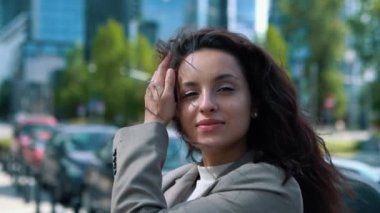 Camera moving back from young pretty businesswoman standing outdoor in city and looking at camera. Beautiful successful woman entrepreneur smiling in street in big city. Business style. Slow motion