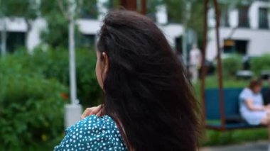 Camera moving around Caucasian beautiful young brunette woman in positive mood standing in street in city typing on smartphone using gadget. Urban lifestyle. Close up shot. Slow motion