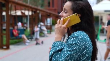 Close up of young woman smiling and speaking on mobile phone. Camera moving around pretty female chatting on cellphone in city outdoor. Urban lifestyle. Leisure. Communication concept