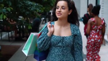 Close up portrait of joyful contented Caucasian female in dress walking in good mood after shopping in city. Positive young woman with bags goes from shopping mall. Happy emotions. Slow motion