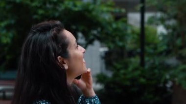 Close up of beautiful young Caucasian woman chatting on smartphone and laughing while walking outdoor. Side view. Attractive cheerful female having conversation on mobile phone call. Leisure concept