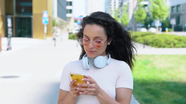 분홍색 안경을 아름다운 거리를 휴대폰으로 타이핑을 있습니다 쾌활하고 머리의 여학생 — 비디오
