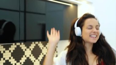 Mutfakta dans edip kulaklıkla müzik dinleyen kırmızı iç çamaşırlı ve beyaz bornozlu mutlu esmer kadını yakından çek. Beyaz tenli güzel bir bayan sabah evde en sevdiği şarkıyı dinliyor.