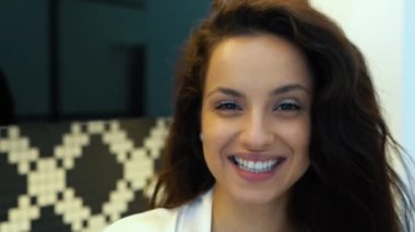 Kamera, mutfakta durup kameraya gülümseyen güzel, neşeli genç bayandan geriye doğru hareket ediyor. Kapatın. Kafkasyalı seksi esmer kadın modern dairede kameraya bakarak gülümsüyor. Yavaş çekim