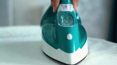 İç mekândaki ütü masasında ütüyle giysileri ütülerken yakın çekim. Evde ütü yapan bir kişi var. Giysileri hazırlamak için yakın çekim. Ev işi. Ağır çekim. Ev işi.