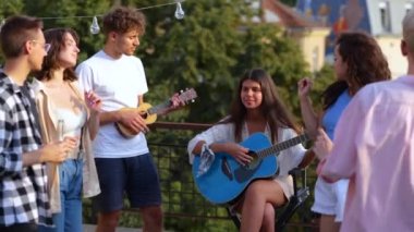 Beyaz mutlu gençler çatıdaki bir partide gitar çalıp dans ederek eğleniyorlar. Kapatın. Müzik çalan kadın ve erkek müzisyenlere yaklaşıyoruz. Arkadaşlar partide müzikten hoşlanırlar. Yavaş çekim