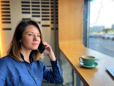 Kafkasyalı neşeli güzel kadının kapalı bir kafede oturup gözlerini kaçırırken cep telefonuyla konuşmasının yakın çekimi. Boş zaman. Kadın cep telefonuyla arıyor. Telefondaki bayan konuşuyor. İletişim konsepti