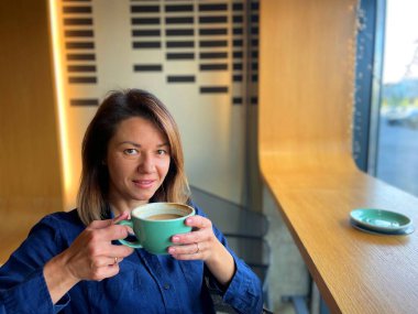 Kahvehanede otururken elinde kahve fincanı tutan ve kameraya bakan mutlu ve çekici bir kadın. Pencerenin yanındaki kafede kahve içen genç ve güzel bir bayan var. Boş zaman. Dinlenme kavramı