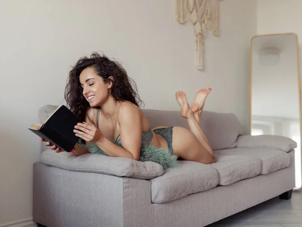 Szczęśliwa Młoda Atrakcyjna Ciemnowłosa Kobieta Leżąca Kanapie Mieszkaniu Czytająca Książkę — Zdjęcie stockowe
