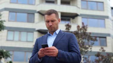 Şehirde ciddi yüzlü beyaz bir erkek müdürün akıllı telefondan mesajlaşırken çekilmiş portresi. Genç başarılı iş adamı cep telefonuyla internette geziniyor. İş hayatı