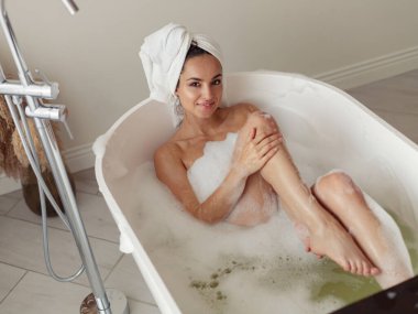 Yüzünde gülümseme olan, köpüklü, gevşetici ve gülümseyen beyaz bir kadın. Güzel bir kadın cesedi küvette suyla yıkıyor. Sabah hijyeni. Temiz vücut