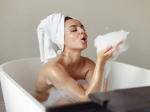 매력적 여자가 수건을 욕조에 위에서 비누를 불면서 근심없는 일과를 즐기는 — 스톡 사진