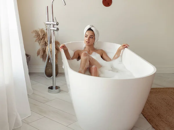 浴室で熱い風呂を楽しみ 離れて見る家の中で若い白人の陽気なかなりの女性 バスルーチン 石鹸泡でお風呂に入る美しい幸せな女性 リラックスした贅沢なコンセプト — ストック写真