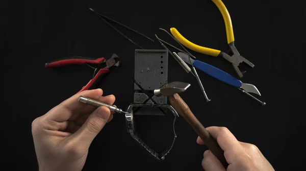 Repairing watch with tools, isolated on black background, repair metal watch by hammer, male watchmaker hand with hardware on a desk, top view