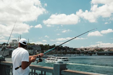 Emininonu Galata Köprüsü 'nde balıkçı, Türkiye İstanbul turizm konsepti, geniş açı, bulutlu hava, beyaz giyen orta yaşlı adam, hobiler ve boş zaman, şehir manzarası