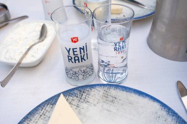 Türk Yeni Rakısı bardakları, masada su, aperatif, geleneksel Türk alkolü, içme konsepti, Yeni Rakı bardağı, oturma manzarası.