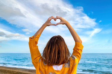 Seni her şeyden çok seviyorum! Kumsalda genç bir kadın ellerini havaya kaldırarak bir kalp çiziyor. Sevgi dolu anılar. 