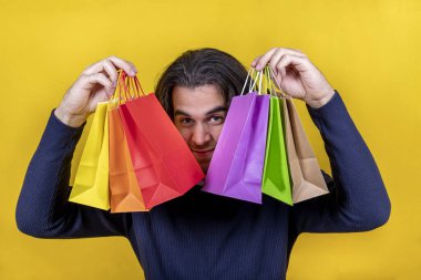 Sürpriz! Parlak sarı arka planda genç bir adam cazip görünüşlü birkaç renkli kese kağıdı gösteriyor. Alışveriş ve hediye konseptleri.