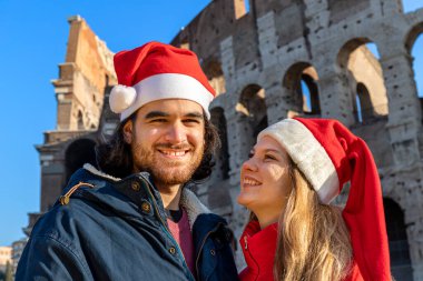 Colosseum 'un önünde kırmızı Noel Baba şapkalı genç bir çift poz veriyor. Mutluluk ve sevgi hissi. Noel tatili kavramı.