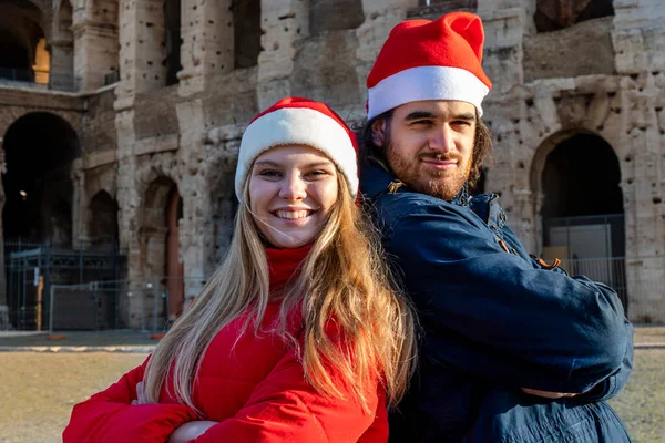 赤いサンタの帽子をかぶったコロッセオの前で写真を撮る素敵な若いカップル 幸せと愛の感覚 クリスマス休暇のコンセプト — ストック写真