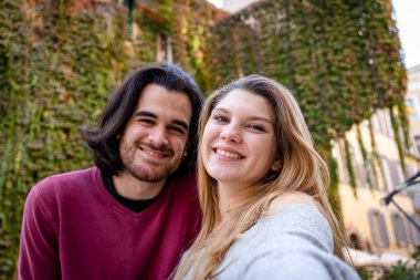 Roma 'ya seyahat eden güzel bir çift. Genç çift tarihi merkezde bir sokakta selfie çekiyor. Arka planda sarmaşıkla kaplı bir bina.