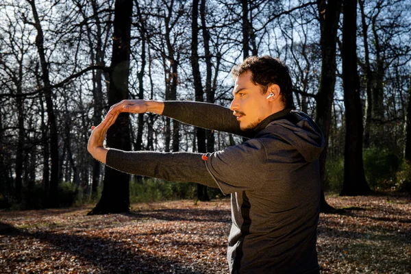 Koşucu ormanda esneme hareketleri yapıyor. Mavi gözlü ve bıyıklı genç adam parkta antrenman yapıyor..