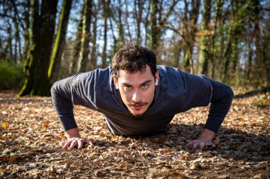 Runner, ormanda şınav çekiyor. Mavi gözlü ve bıyıklı genç adam müziği dinlerken yerde şınav çekiyor..